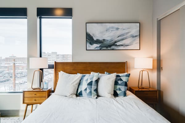 Modern bedroom featuring a bed with decorative pillows and large windows overlooking a cityscape.