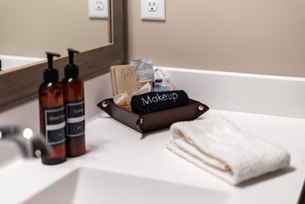 A bathroom counter with labeled lotion bottles, a tray for makeup, and a folded towel.