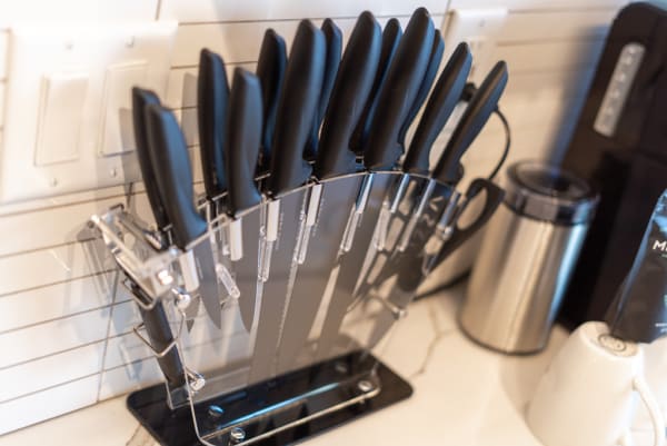 A knife block with multiple black-handled knives in a kitchen environment.