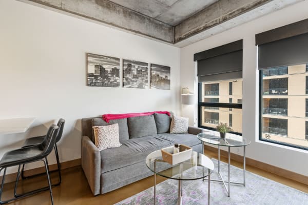 Modern living room with a gray sofa, glass tables, and city skyline artwork.
