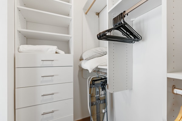 Modern walk-in closet with white shelves, drawers, hangers, and pillows.