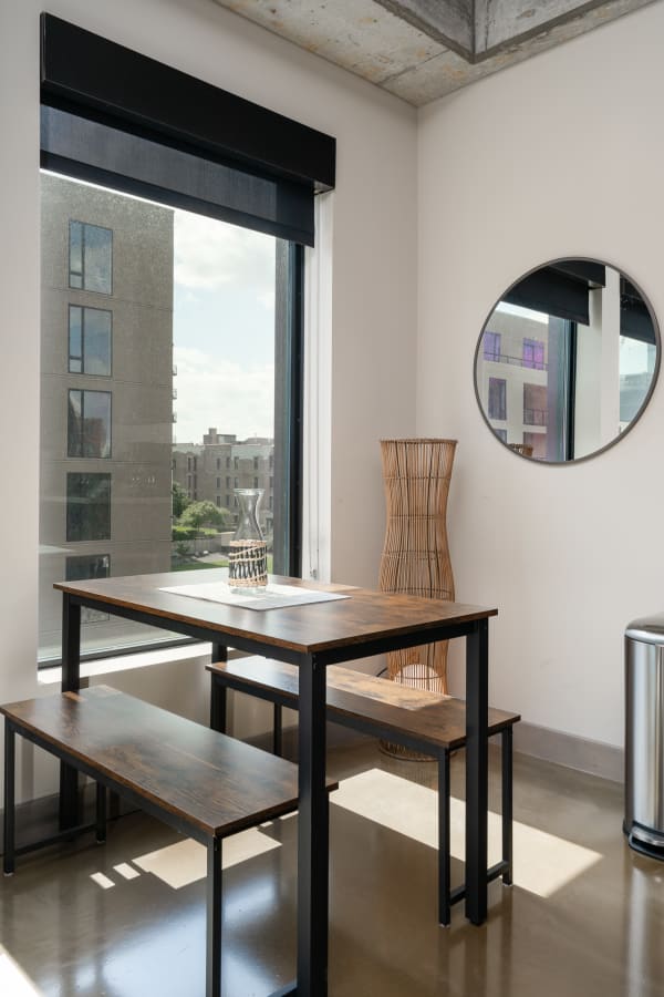 Modern dining nook featuring a wooden table, benches, a decorative vase, and large windows with an urban view.
