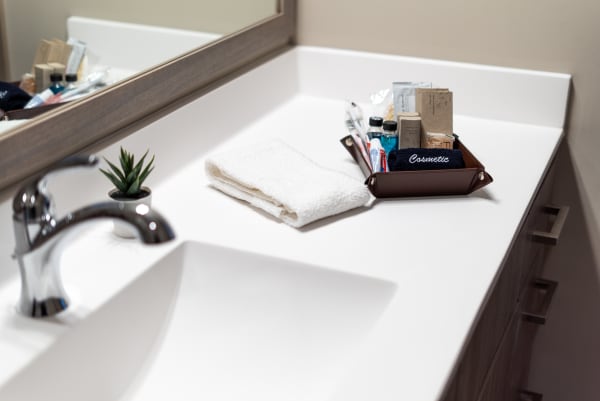 White bathroom countertop with a folded towel, small plant, and a tray of cosmetics.