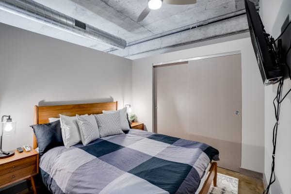 Modern bedroom featuring a cozy bed with a patterned quilt, a minimalist lamp, and an industrial-style ceiling.