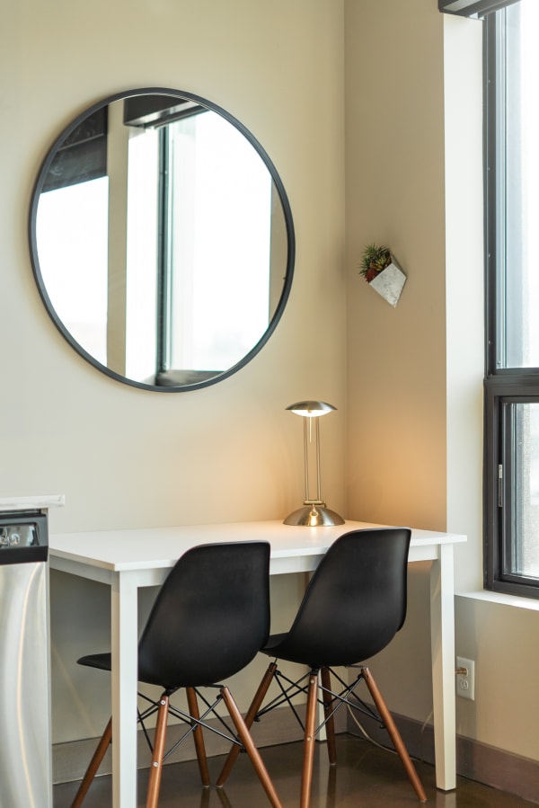 Minimalist corner workspace with a round mirror, a desk lamp, and a planter.