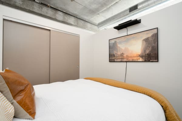 Modern bedroom featuring a bed with white coverlet and mustard bedspread, and a framed artwork on the wall.
