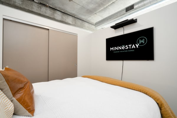 Modern bedroom with white bedding, mustard throw, and wall-mounted TV.