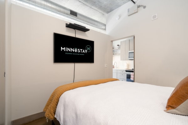 Interior of a vacation home featuring a bed and a TV displaying MINNēSTAY logo.