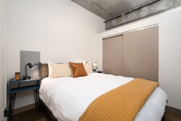 Minimalistic bedroom with a neatly made bed, mustard quilt, and modern furniture.