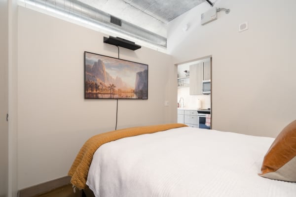 Cozy bedroom with a white bed and orange throw, featuring a mountain landscape painting on the wall.