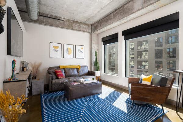 A stylish living room with a leather sofa, geometric art, and a blue striped rug.