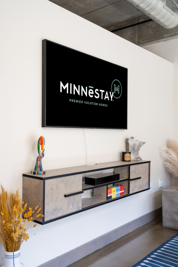 Modern living space with a media console, colorful figurine, and MINNēSTAY logo on TV.