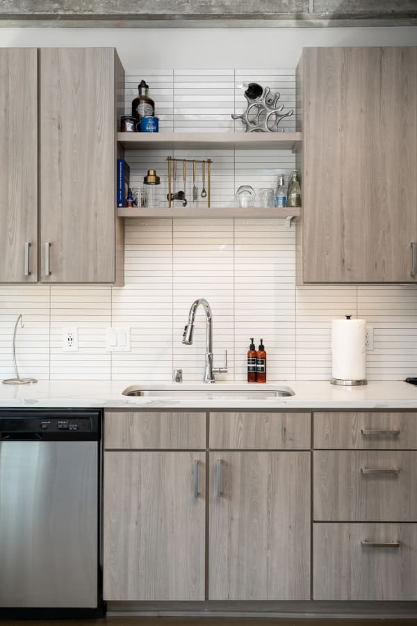 Contemporary kitchen with gray cabinets, a white stone sink, and decorative items on shelves.