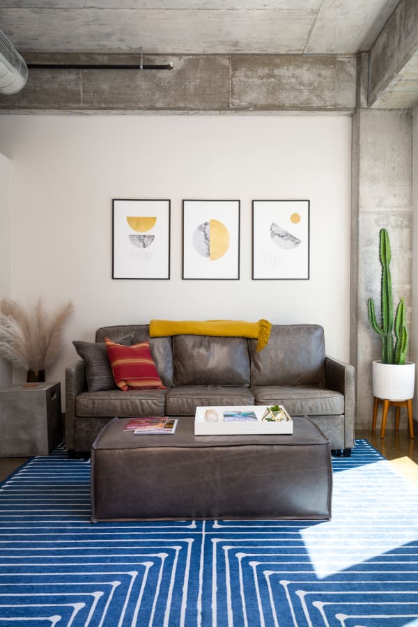 Cozy living room with a gray leather couch, striped red and yellow cushions, a cactus, and modern art on the walls.