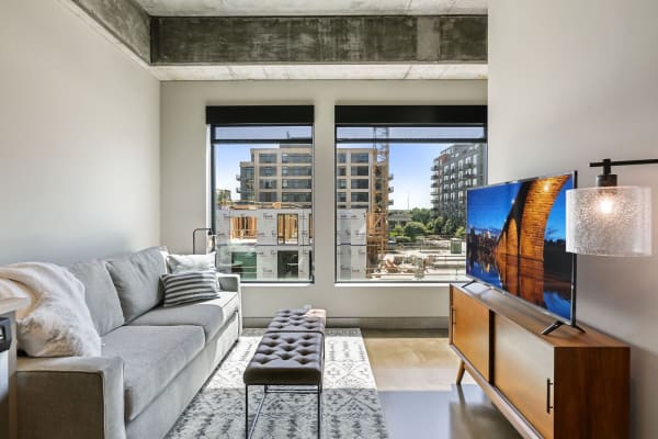 Stylish living room featuring a grey sofa, a tv, and large windows with a view of construction.