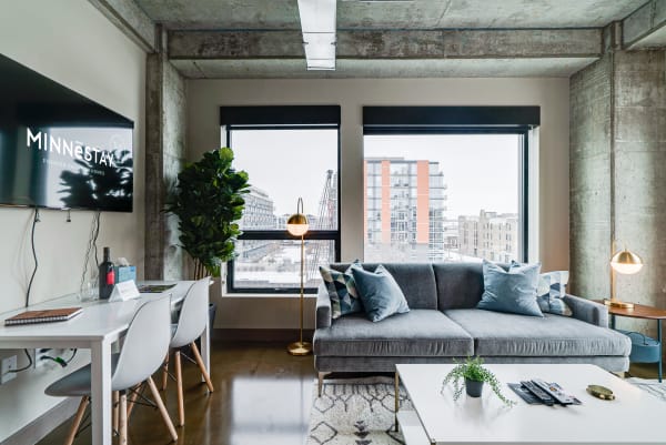 Modern living space with gray sofa, large windows, and urban view.