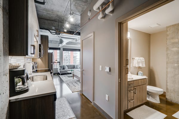 Interior view of a contemporary apartment showcasing a kitchenette, living room, and bathroom area.