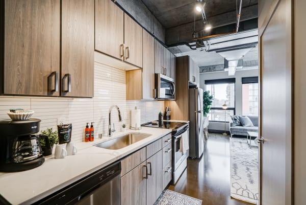 Modern kitchen with light wood cabinetry, white countertop, and a cozy living area in the background.