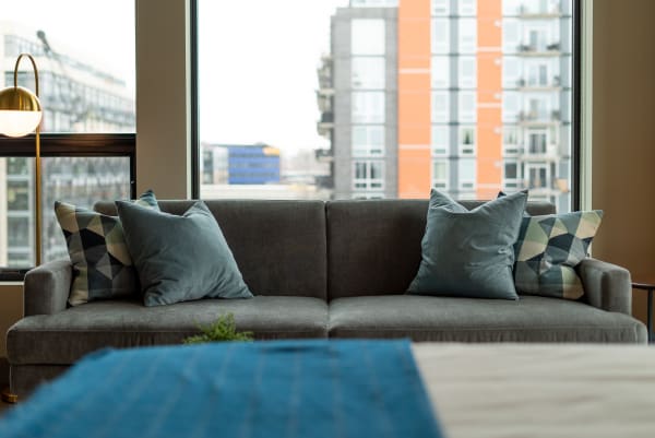 A gray sofa with blue and patterned pillows in front of large windows overlooking a cityscape.