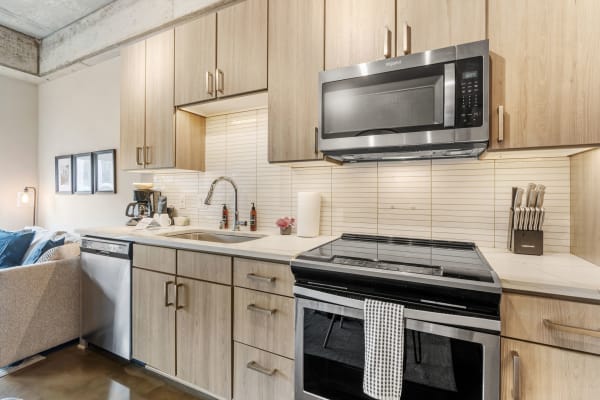 Modern kitchen with light wood cabinets, stainless steel appliances, and a cozy living area.