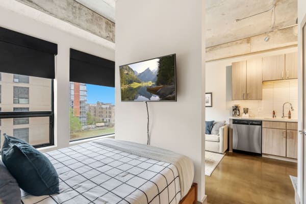 Interior of a modern studio apartment featuring a bed, TV, and kitchenette.