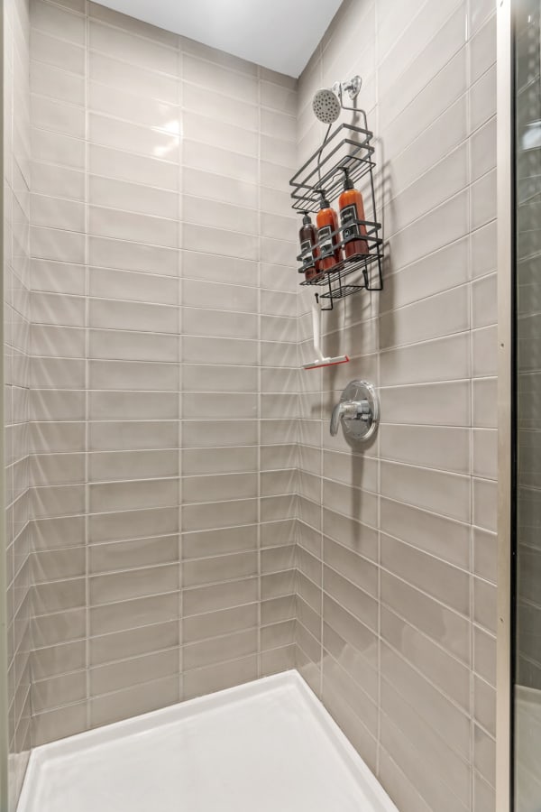 A contemporary shower space with light beige tiles and a metal caddy holding bottles.