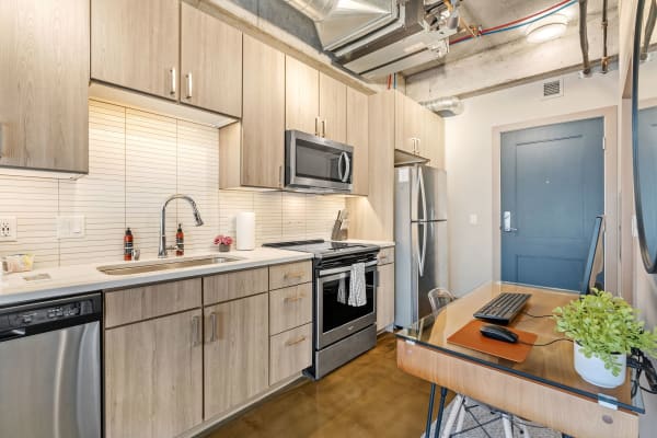 Modern kitchen featuring light wood cabinetry, stainless steel appliances, and a glass-top desk.