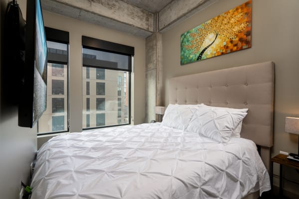A modern bedroom with a white bedspread, beige headboard, and colorful artwork.