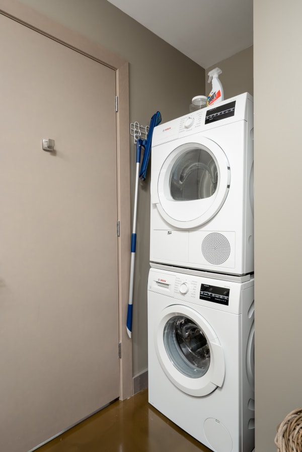 Stacked Bosch washer and dryer in a small laundry space with cleaning supplies nearby.