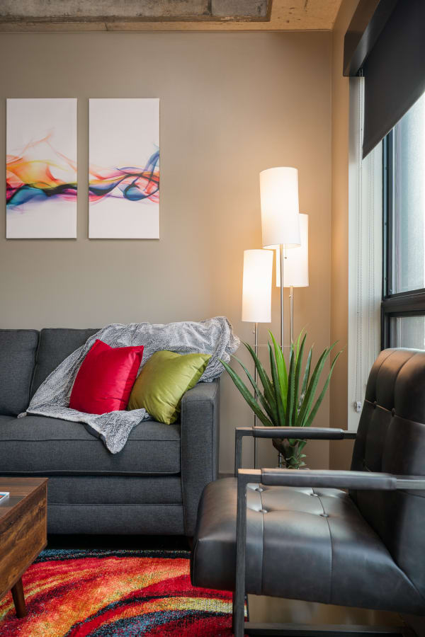 A stylish living room featuring a gray sofa with colorful cushions, abstract artwork, and a floor lamp.