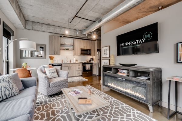 Modern living room in an urban apartment with a gray sofa, armchair, and kitchen area.