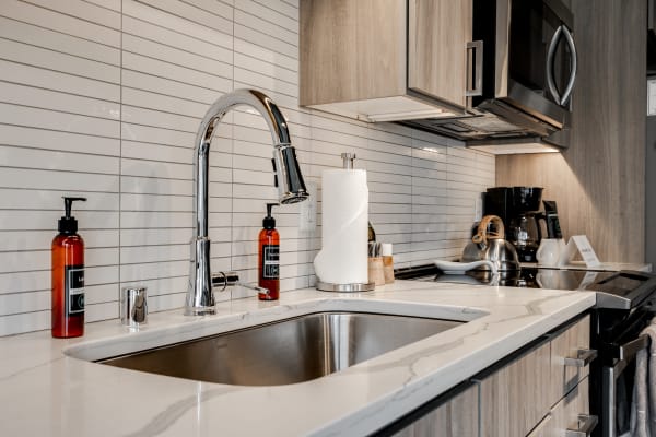 A stylish kitchen sink with a chrome faucet, amber soap dispensers, and a paper towel holder on a marble countertop.
