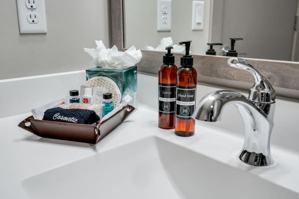 A modern bathroom countertop with lotion, hand soap, a washcloth, and toiletries in a tray.