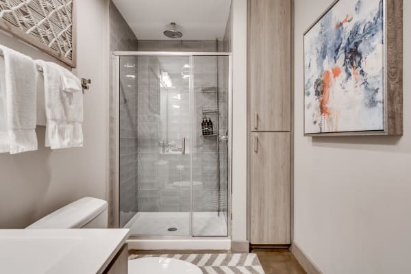 Modern bathroom with glass shower, towels, and abstract art.