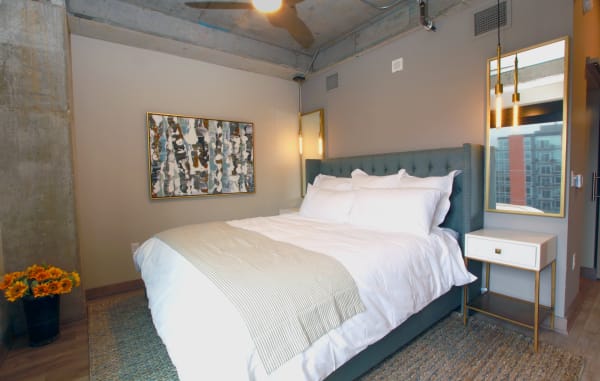 Modern bedroom with a tufted bed, decorative art piece, and flowers in a vase.