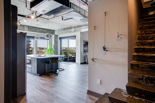 An open-plan modern loft with a kitchen island, large windows, and climbing figurine art on the wall.