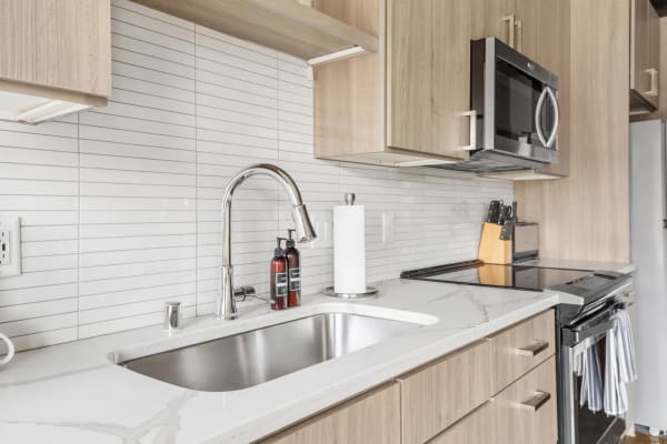 A contemporary kitchen with a marble countertop, stainless steel sink, and wooden cabinets.