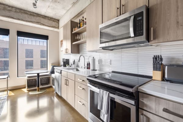Modern kitchen with light wood cabinets, stainless steel appliances, and a round dining table by a window.