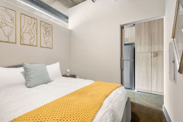 Stylish bedroom featuring abstract art, a neatly made bed, and a glimpse of a kitchen.
