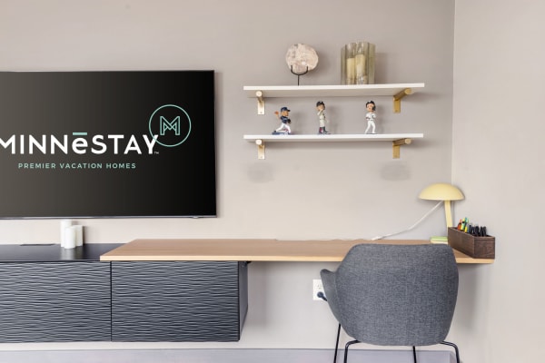 Modern workspace with a TV displaying MINNĒSTAY logo, a wooden desk, and decorative elements.