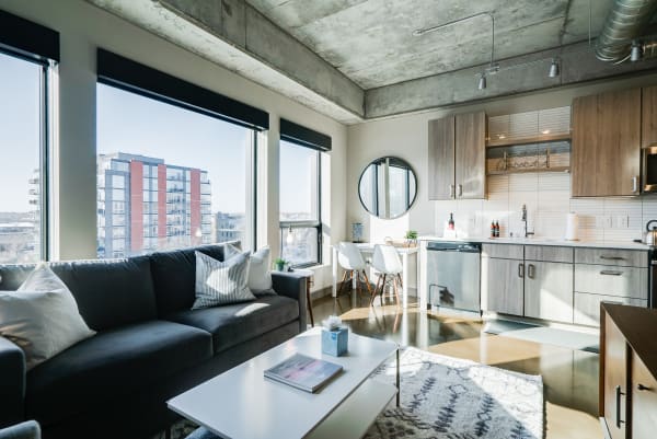 Modern apartment interior with a grey sofa, white coffee table, and a stylish kitchen.