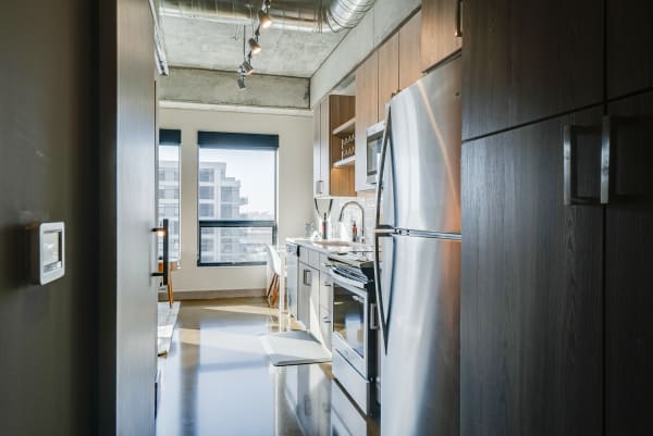Modern kitchen with stainless steel appliances and a small dining area, viewed from a hallway.