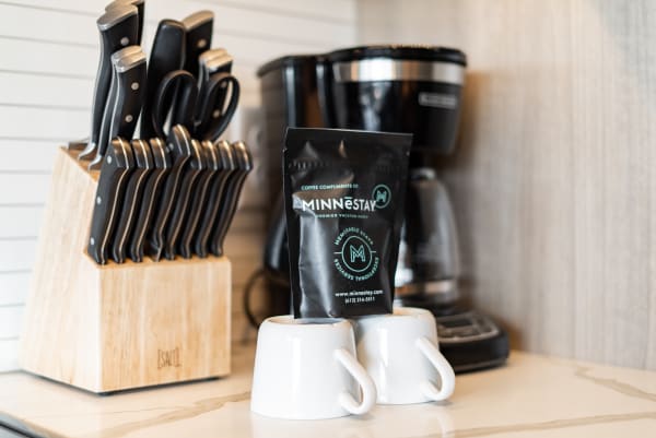 A kitchen counter displaying a MINNESTAY coffee bag, white cups, and a knife block.