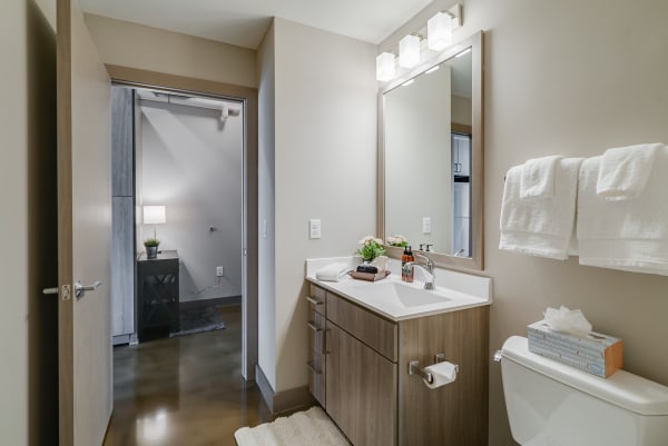 A contemporary bathroom featuring a wooden vanity, mirror with lights, and soft towels.