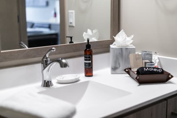 A bathroom countertop featuring hand soap, beauty products, and a decorative tissue box.