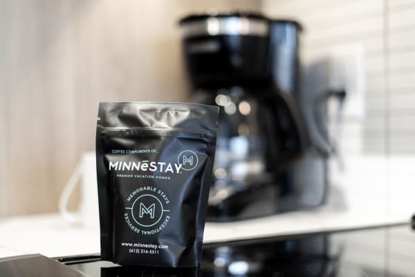 A black coffee bag from MINNĒSTAY with a coffee maker blurred in the background.