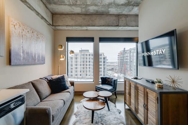 Stylish living room featuring a gray sofa, circular wooden coffee tables, and large windows with a view of surrounding buildings.
