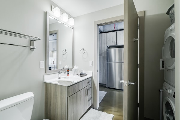 Interior view of a modern bathroom featuring a vanity, mirror, and laundry area.