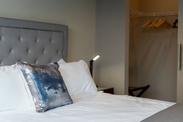 Modern hotel room featuring a made bed with decorative cushions and closet space.