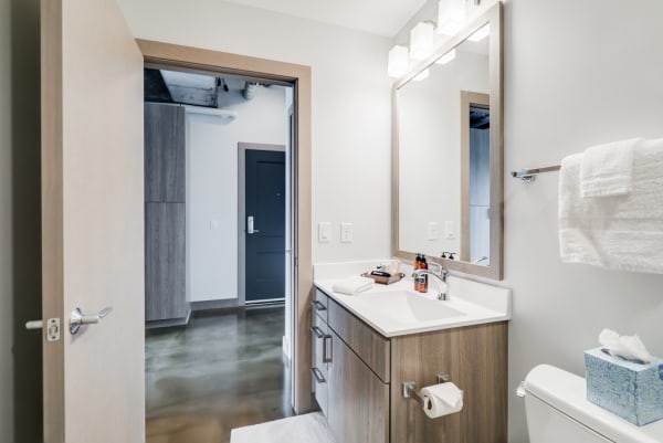 Modern bathroom with white countertops, wood cabinetry, and polished concrete floors.